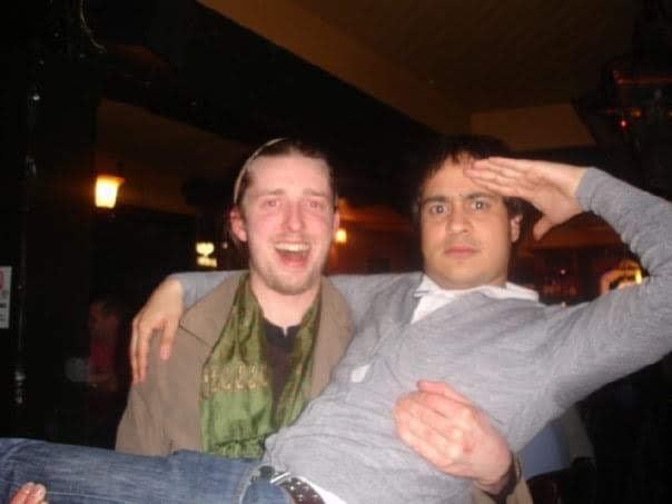 Flav carrying Ricky in a pub. Flav is carrying Ricky chest height, while Ricky has one arm over Flav's shoulder and saluting with his other arm.